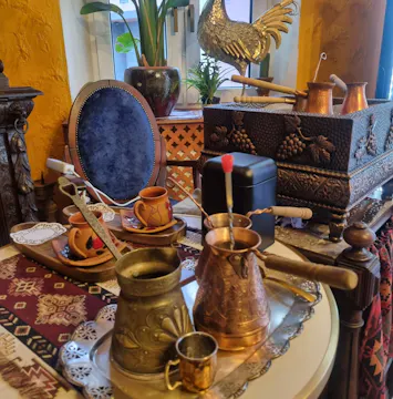 Zestaw mosiężnych i miedzianych naczyń do parzenia kawy na ozdobnym stole w stylu orientalnym.