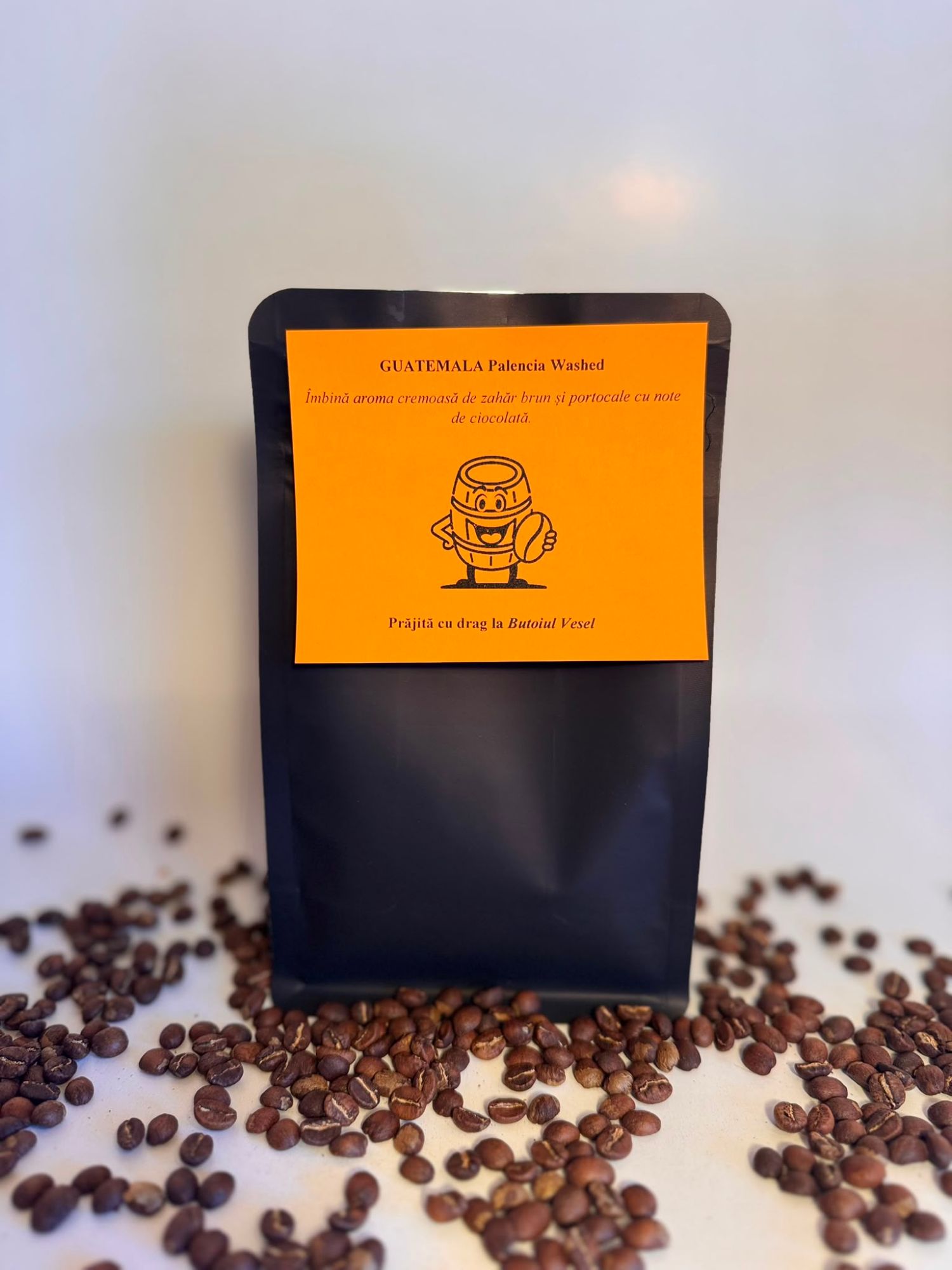 Pachet de cafea Guatemala Palencia Washed, cu boabe prăjite, pe un fundal portocaliu, alături de boabe de cafea.