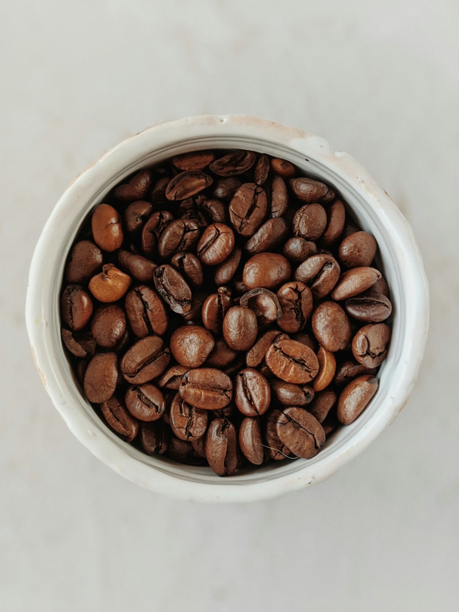 Bucată de cafea prăjită în bol alb, pe un fundal neutru.
