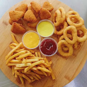 Talerz ze smażonymi nuggetsy, frytkami, krążkami cebuli i sosami: ketchup, musztarda, majonez.