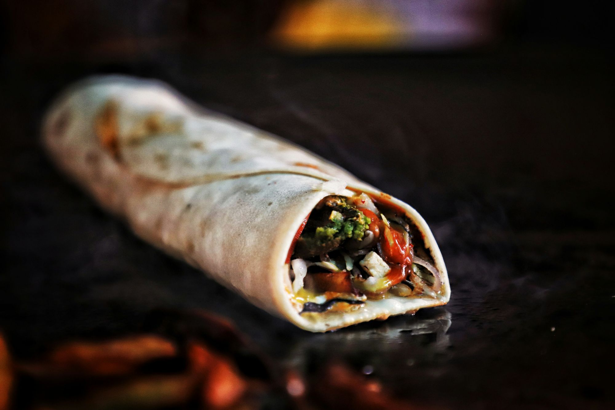 Tortilla rulată umplută cu legume proaspete și sos, aburindă pe un grătar.