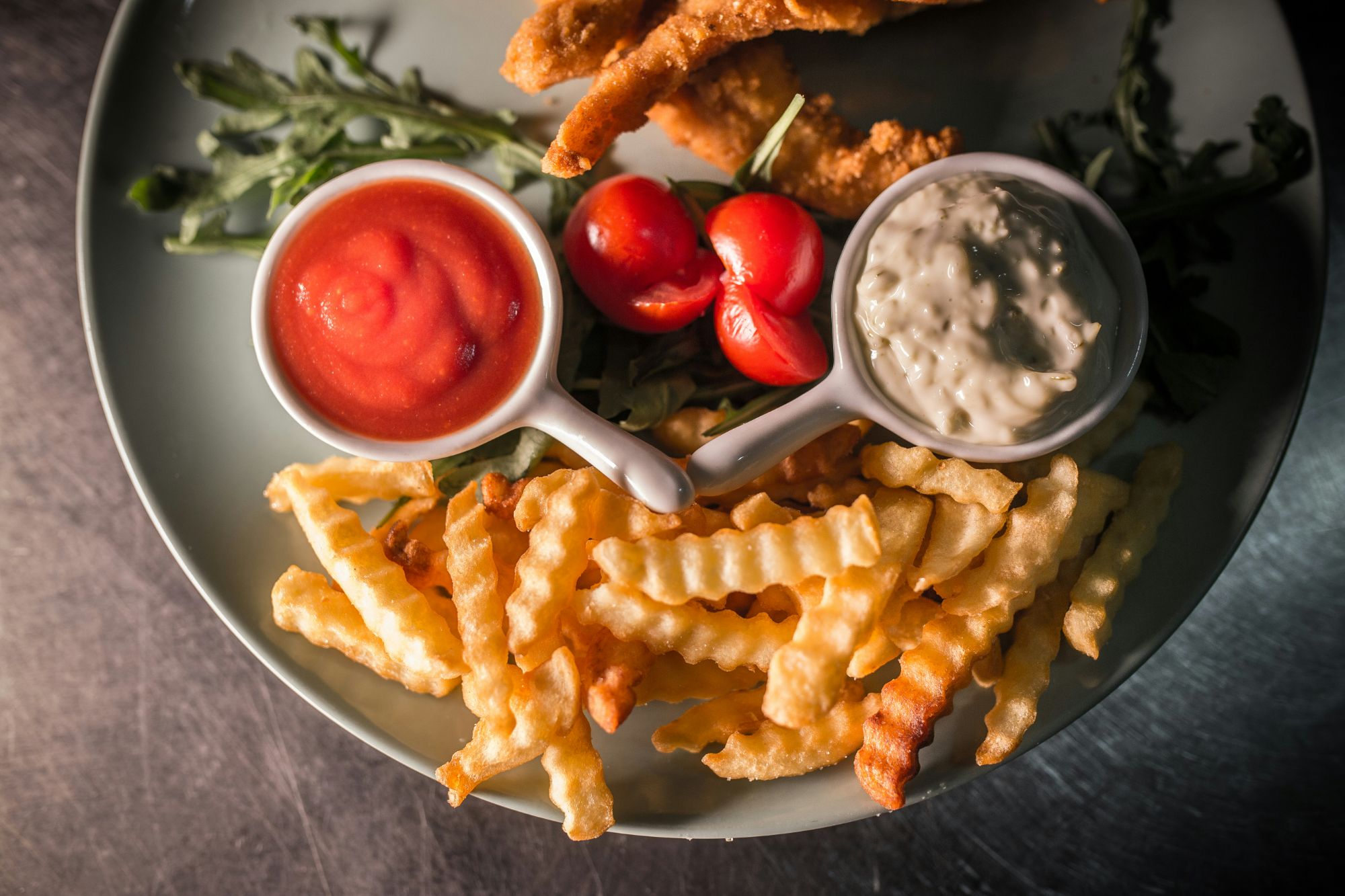 Ținută din cartofi prăjiți crinkle, ketchup și sos de maioneză, alături de bucăți de pește prăjit și roșii cherry.