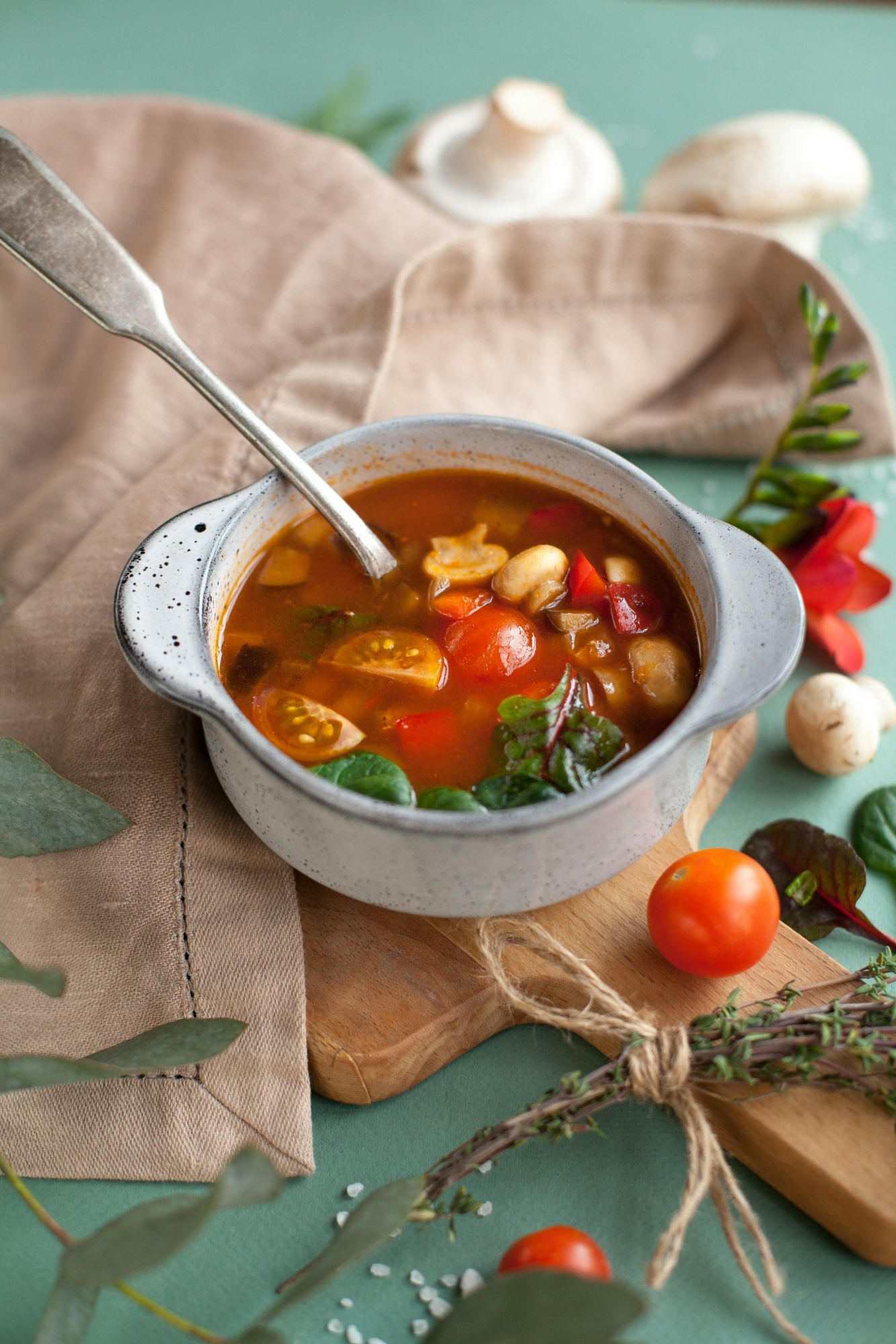 Ciorbă delicioasă cu legume, servită într-un bol pe un fundal de textile și plante.