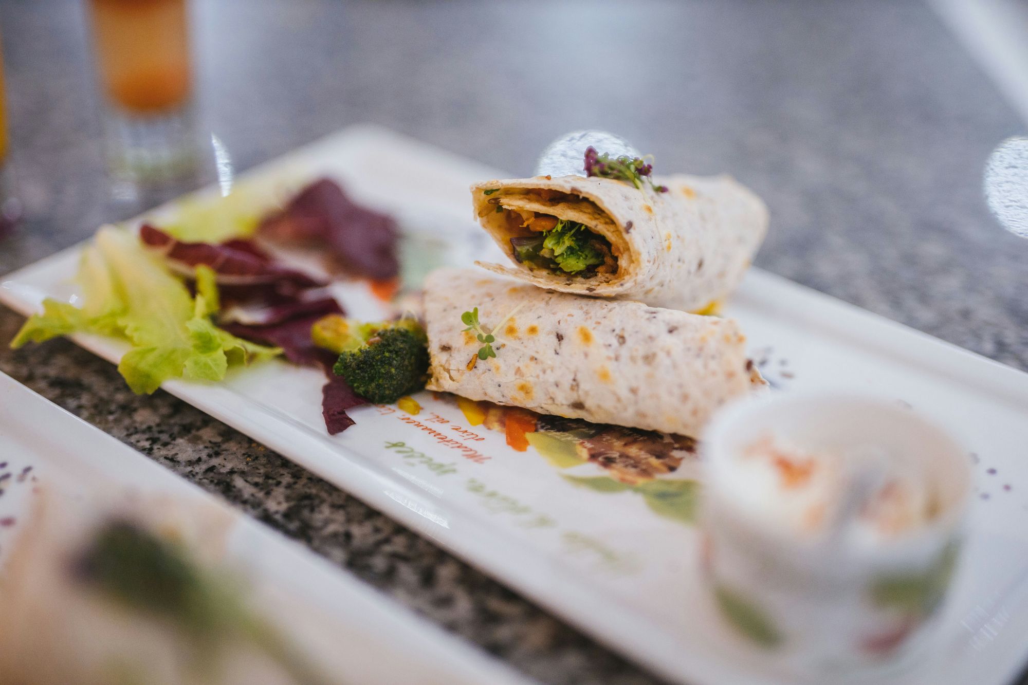 Wrap cu legume pe un platou, alături de salată proaspătă și sos.