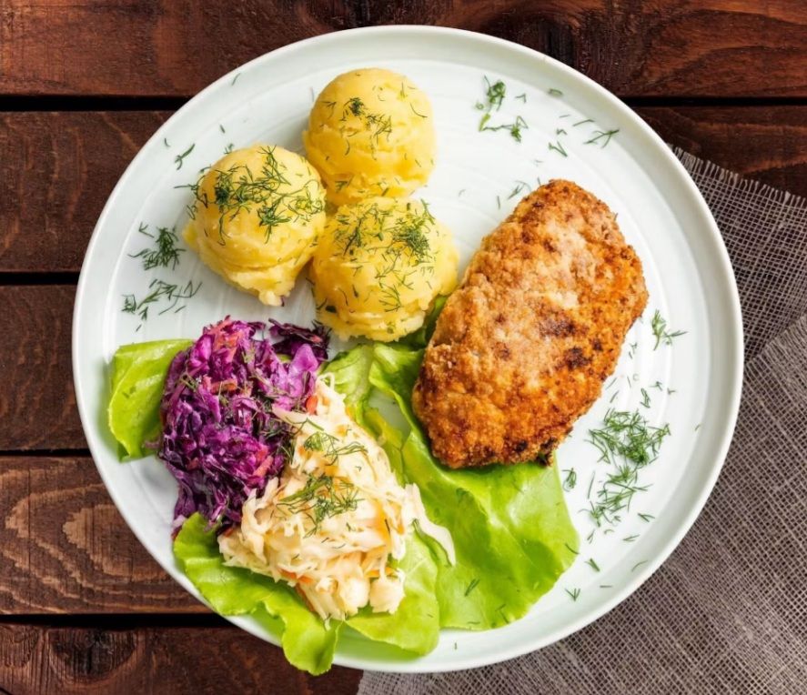 Pyszny obiad: kotlet, ziemniaki, surówki z kapusty i sałaty na talerzu.
