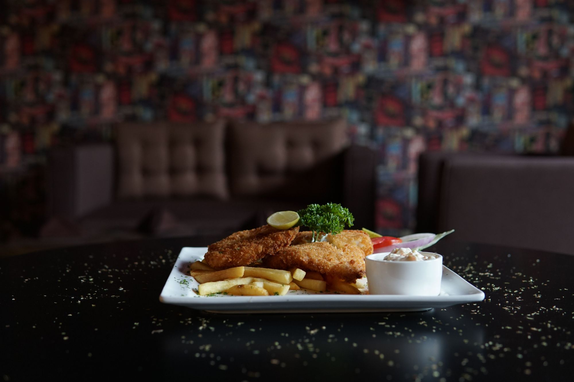 Dania na talerzu: smażony filet rybny, frytki, świeża sałatka i sos. Tło w przytulnej restauracji.