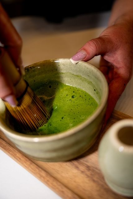 Ručné šľahanie matcha čaju v keramickej miske s bambusovým metličkom.