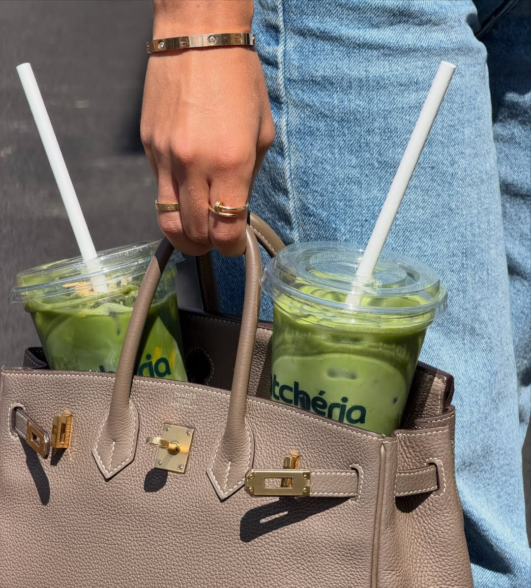 Osoba drží kabelku so zelenými smoothies a bielymi slamkami.