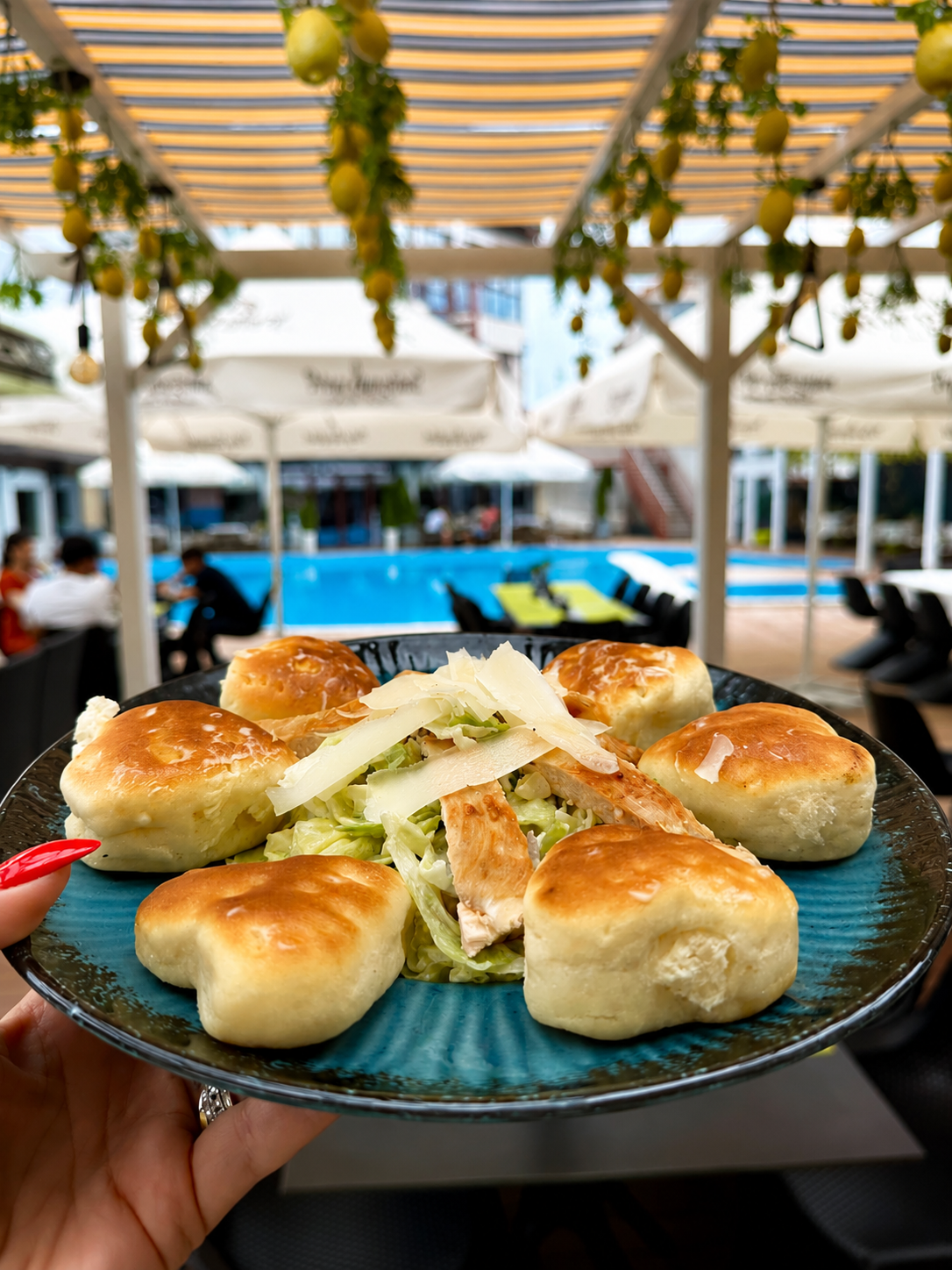 Platou cu chifle umplute, salată de varză și carne, servite lângă o piscină într-un restaurant.