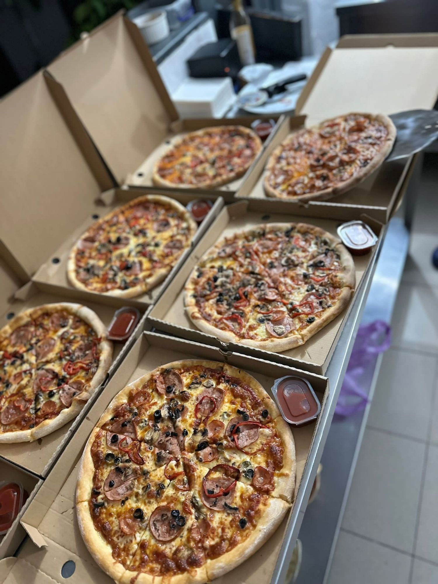 Mai multe pizza delicioase în cutii, cu toppinguri variate, așezate pe o masă.