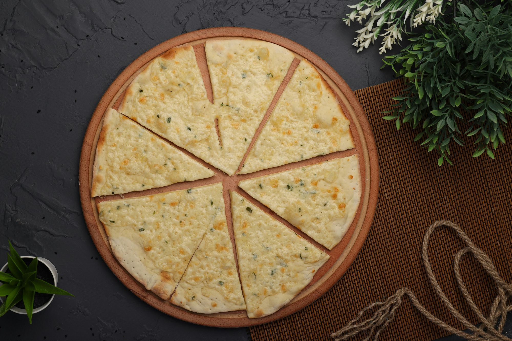 Pizza cu brânză tăiată în opt felii, așezată pe o tavă de lemn, pe un fundal texturat de culoare închisă.