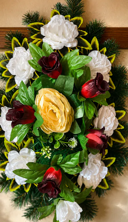 Aranjament floral decorativ cu trandafiri roșii, crini albi și o floare galbenă pe un fundal verde.