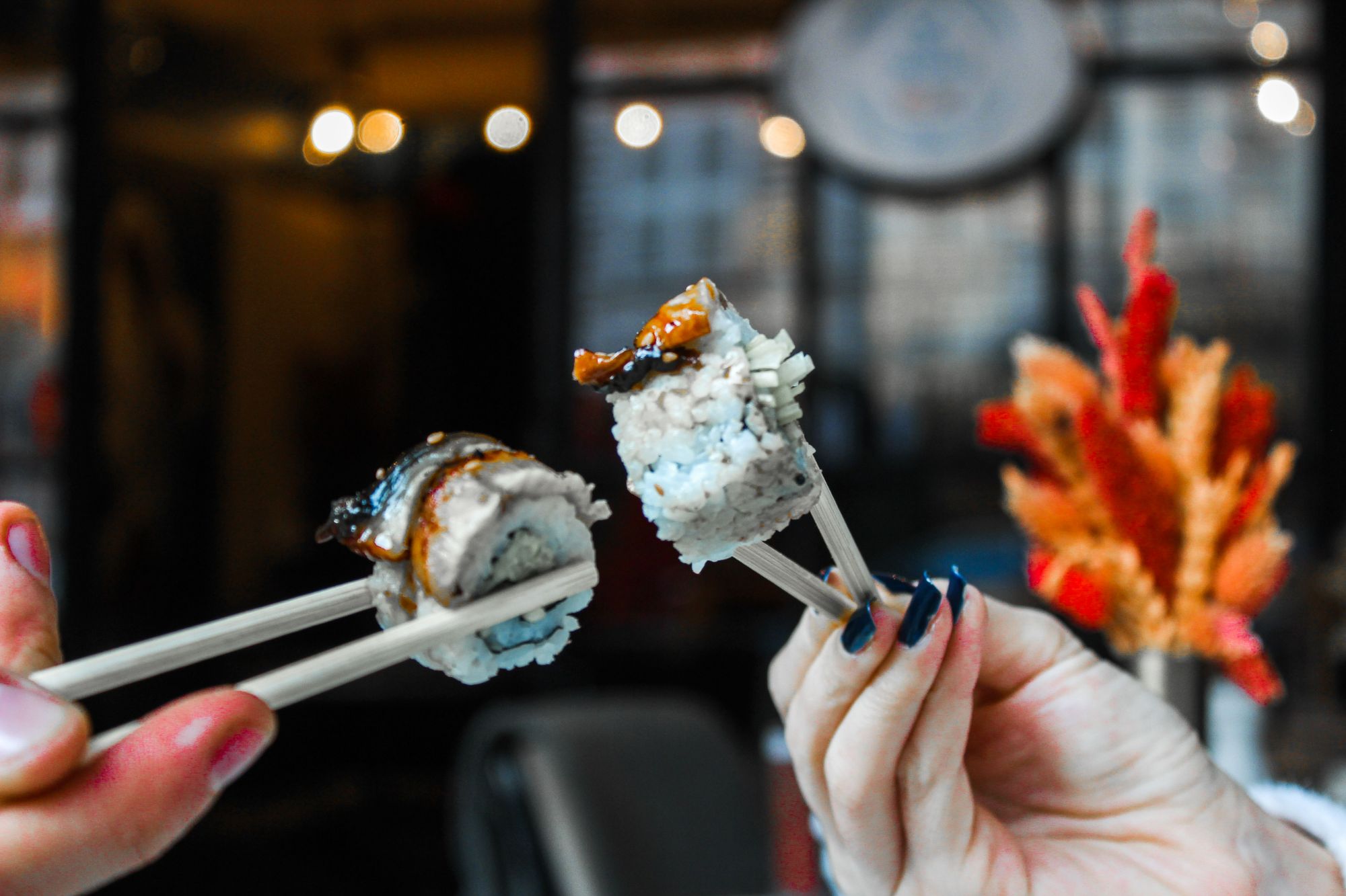 Osoba trzymająca pałeczki, jedząc sushi w restauracji, z kolorowym tłem i dekoracjami.