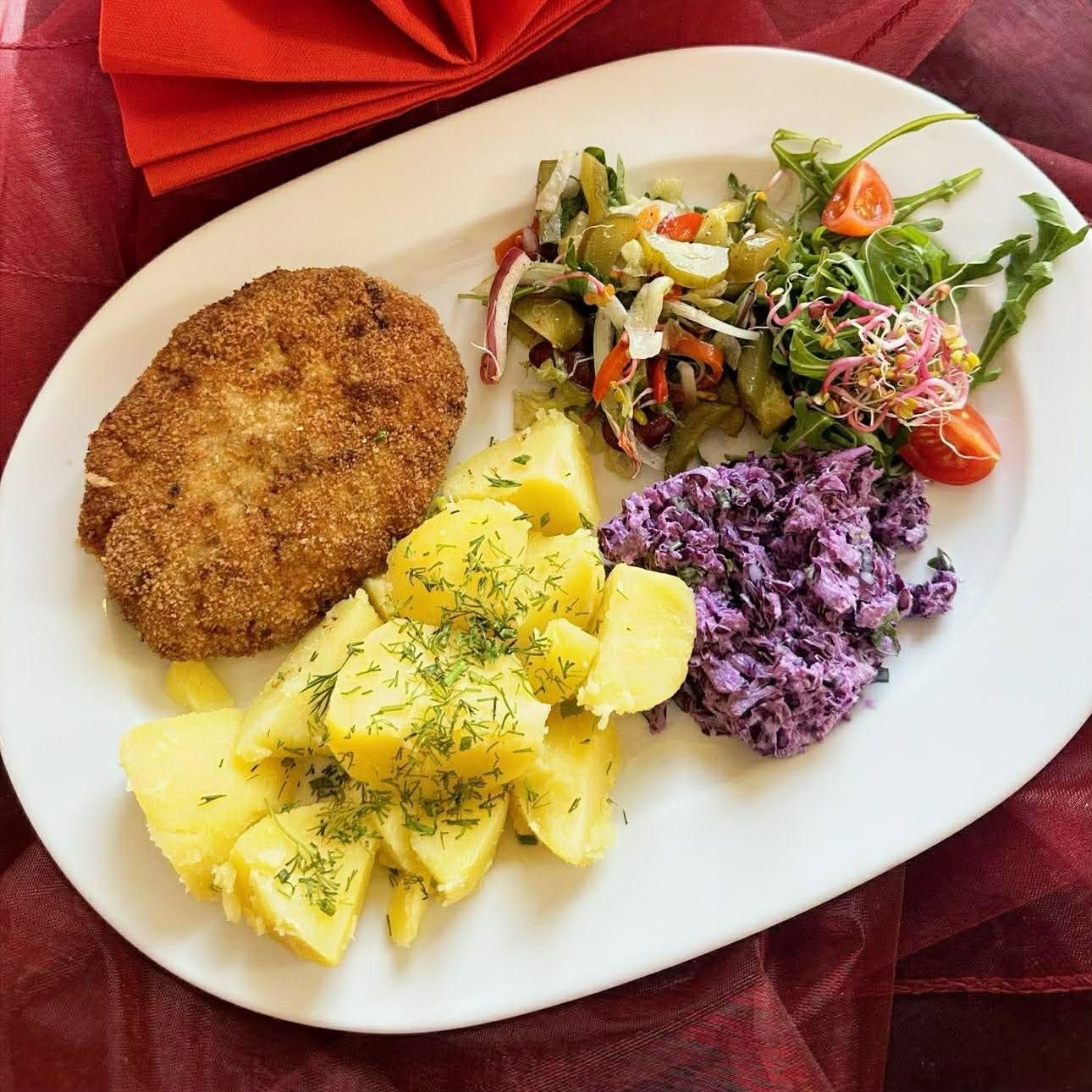 Ziemniaki, surówka, purée z czerwonej kapusty i kotlet schabowy na białym talerzu.
