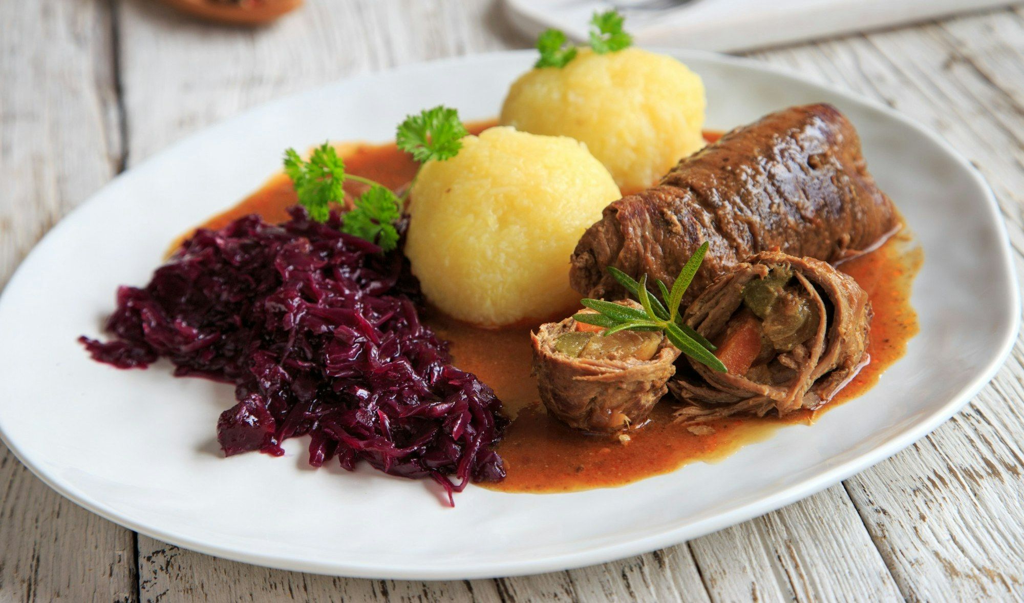 Zrazy wołowe z sosem, puree ziemniaczanym i czerwoną kapustą na białym talerzu.