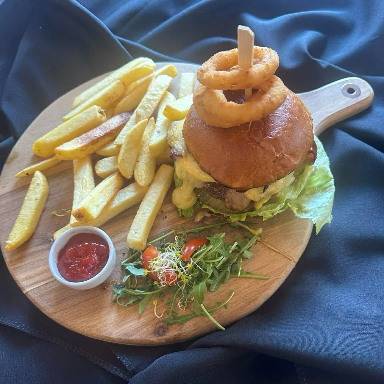Burgery z frytkami, sosem pomidorowym oraz sałatą, serwowane na drewnianej desce.