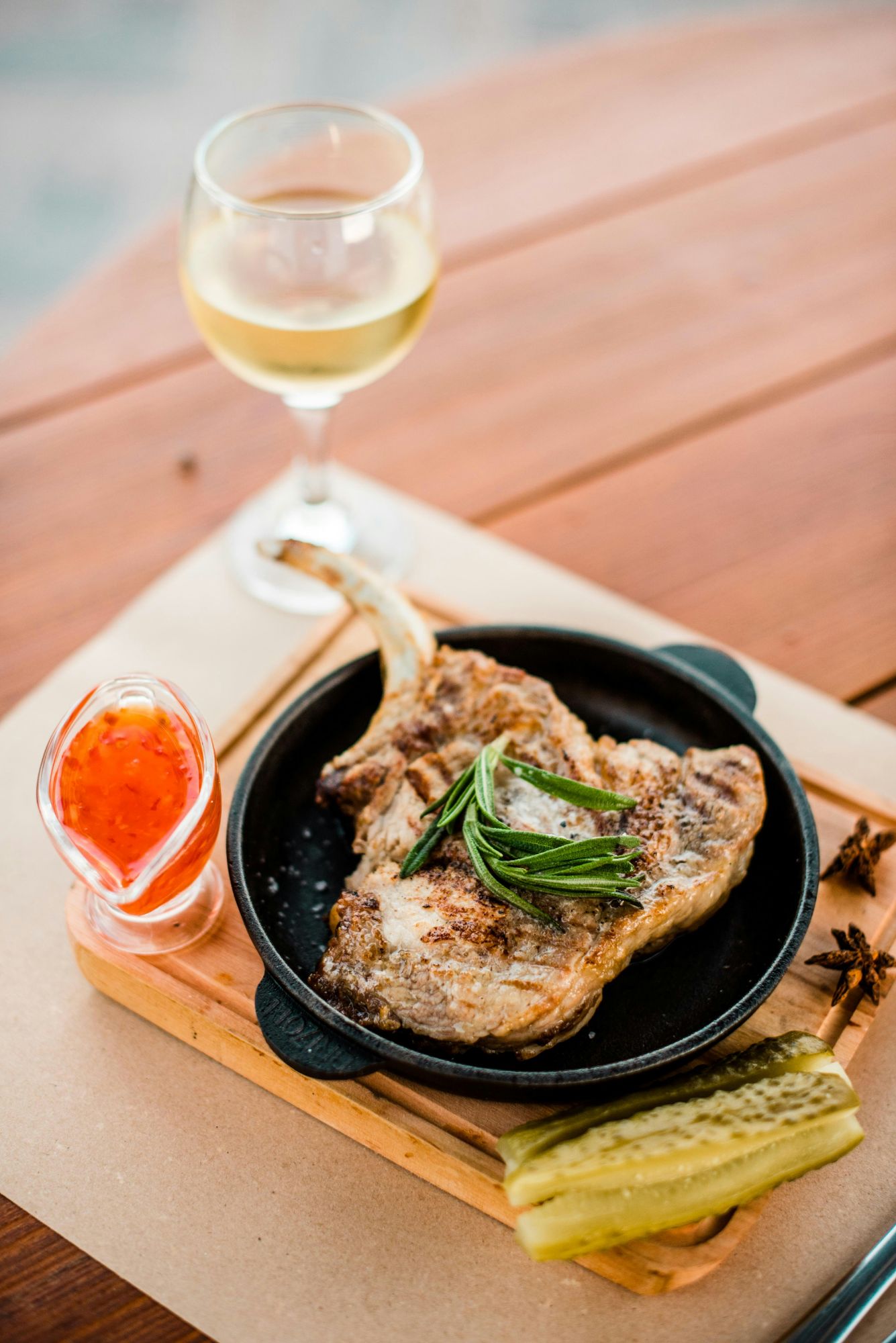 Friptură de porc pe farfurie, cu sos, castravete și pahar de vin alb alături.