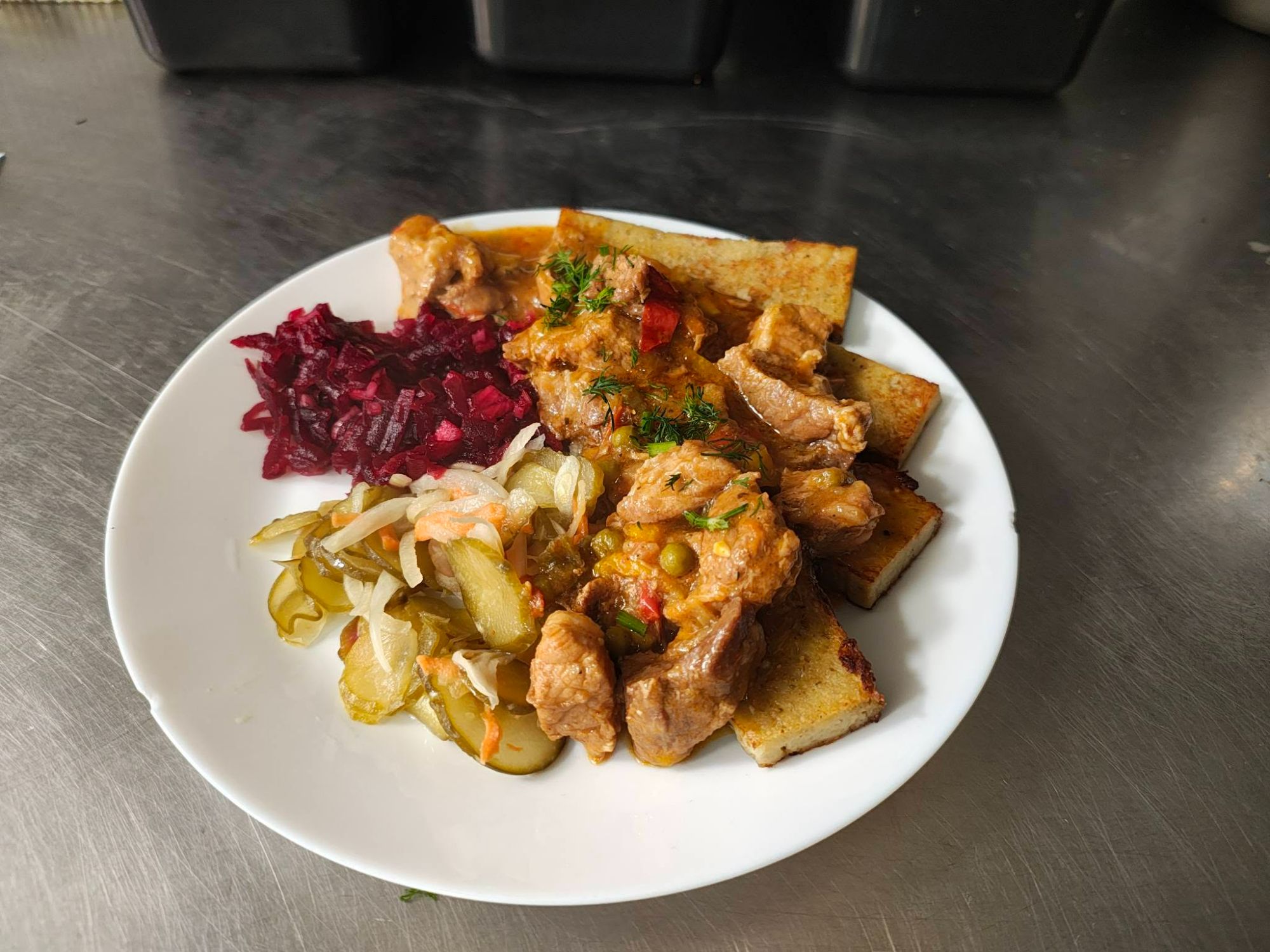 Talerz z duszonym mięsem, pieczonym chlebem, surówką z ogórków i sałatką z buraków.