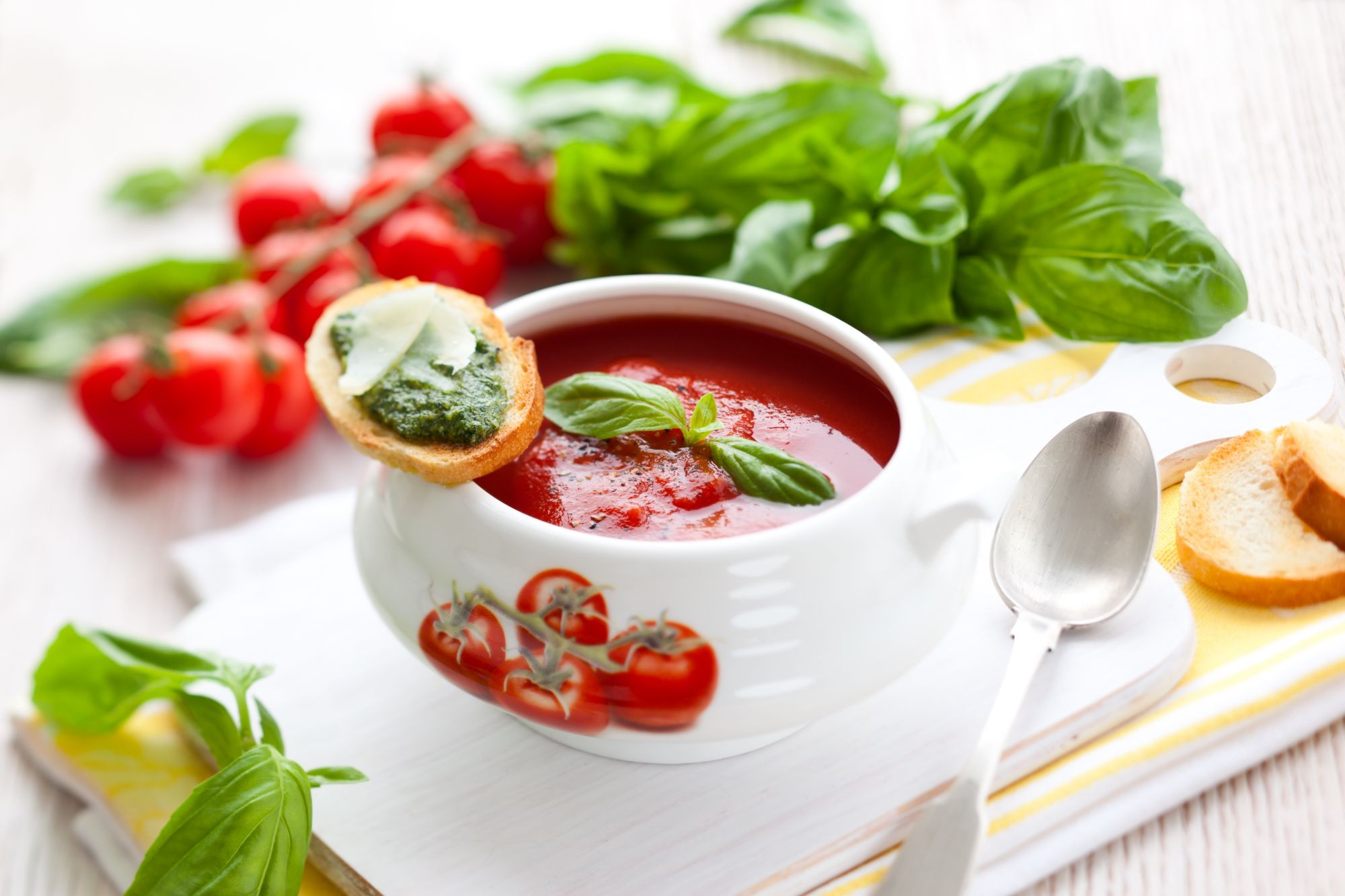 Zupa pomidorowa w białej misce z liściem bazylii, następnie grzanka z pesto i świeżą bazylią obok.