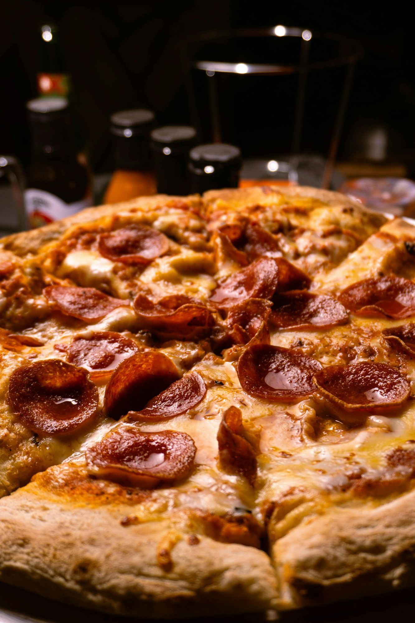 Pizza z pepperoni na talerzu, z napięciem na serze i cienkim cieście, w tle butelki napojów.