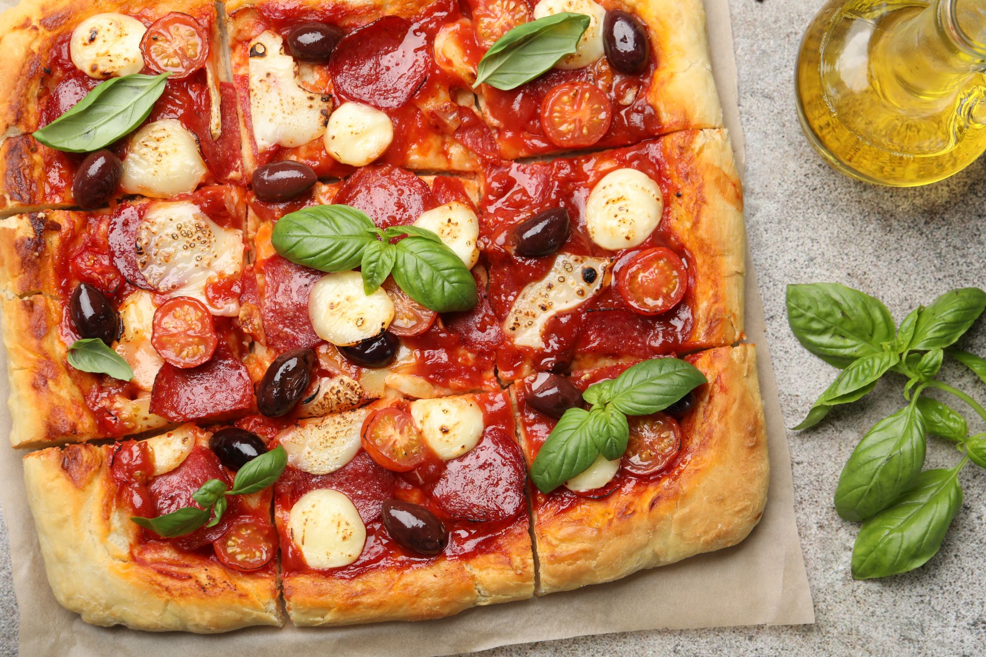 Pyszna pizza z pepperoni, pomidorami cherry, oliwkami i świeżą bazylią na złotym cieście.