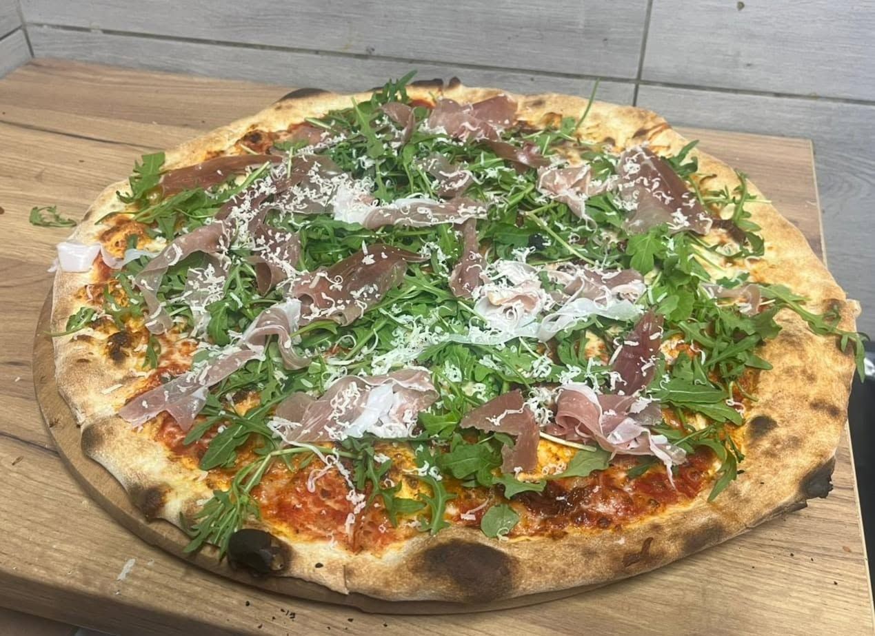 Pizza z rukolą, szynką parmeńską i serem na drewnianym blacie.