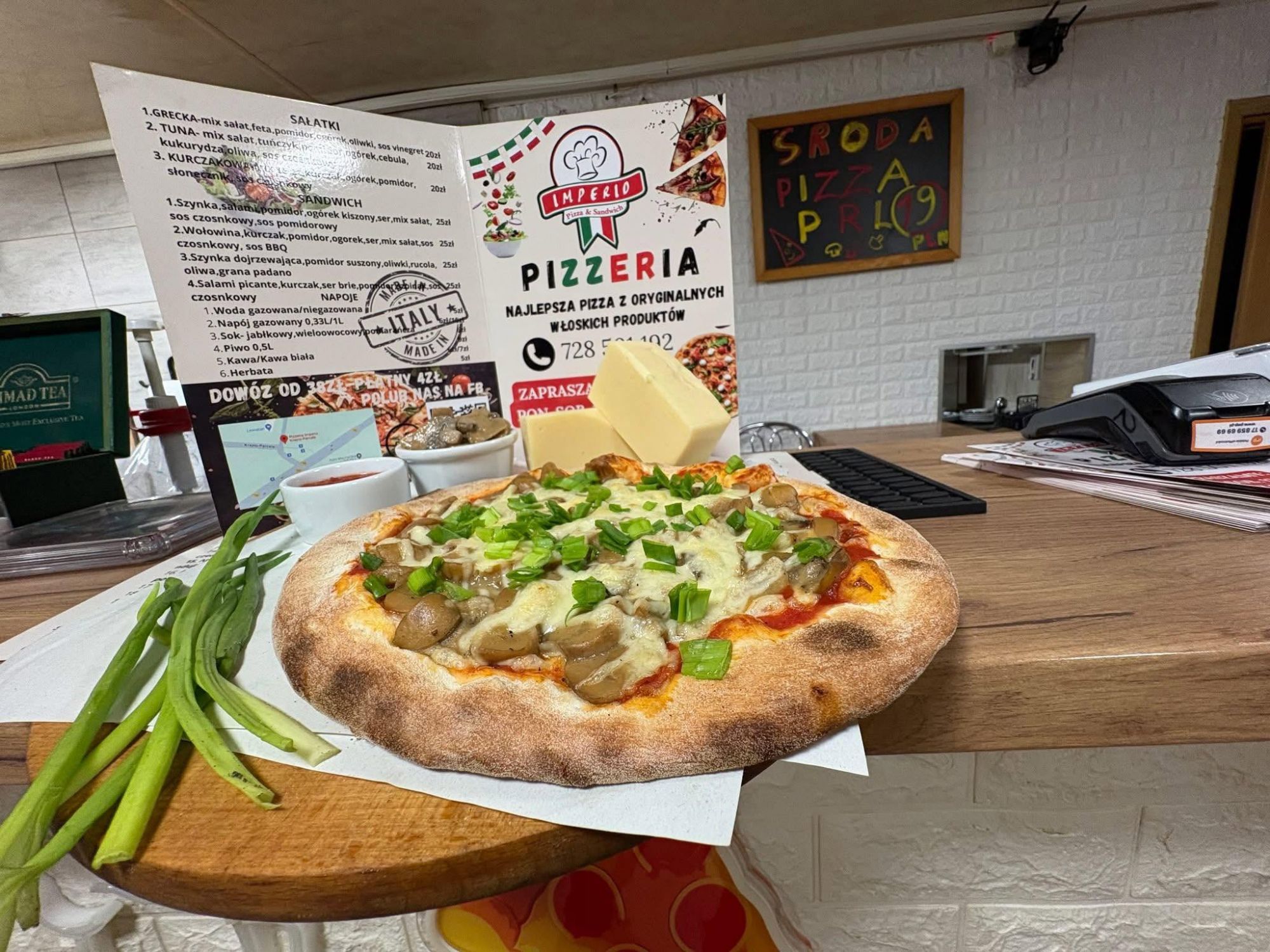 Pyszna pizza z grzybami, cebulą i serem w pizzerii, z menu i kawałkiem masła w tle.