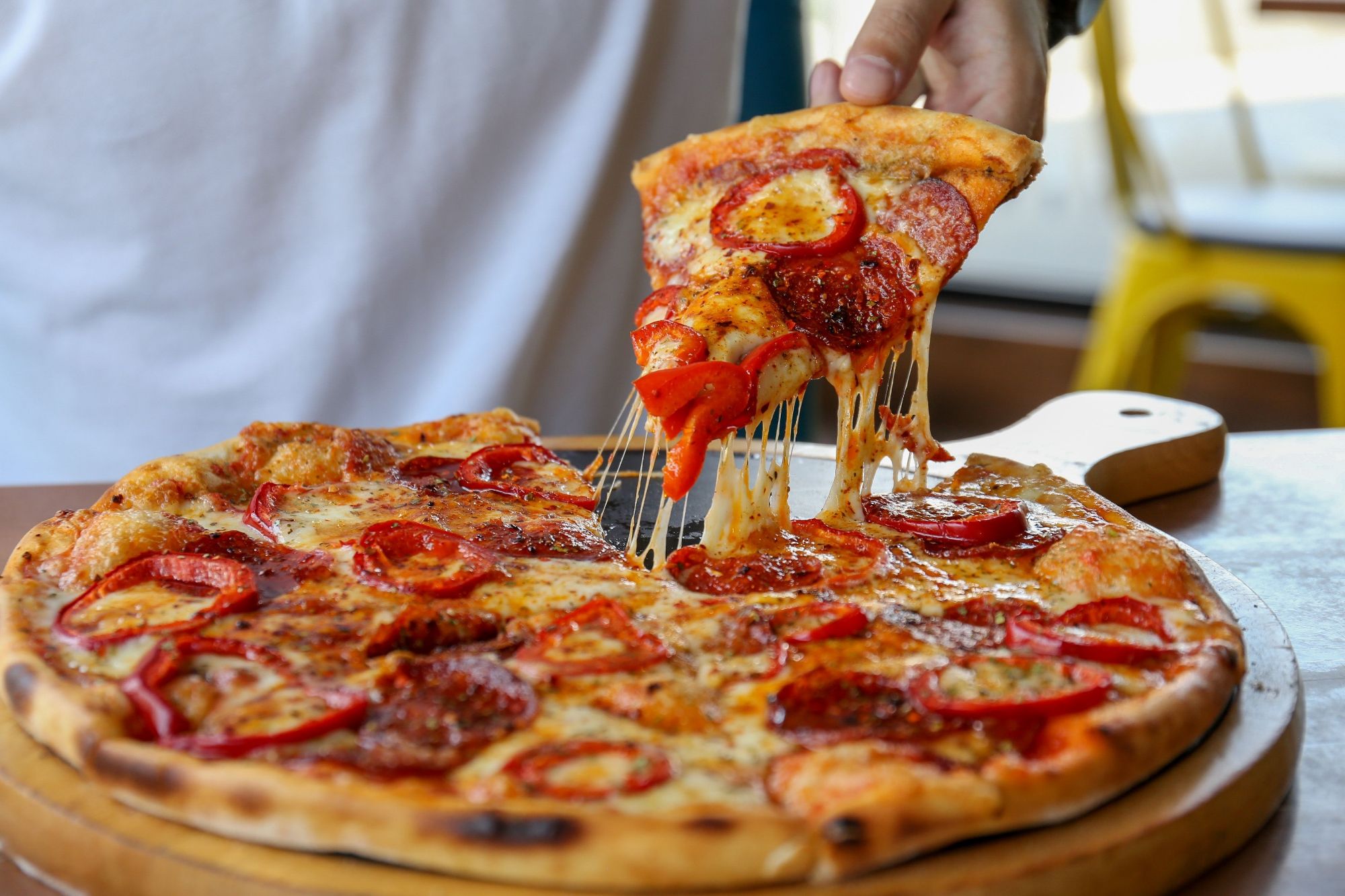 Pizza z pepperoni i papryką, kawałek wyciągany z okrągłej pizzy na drewnianej desce.