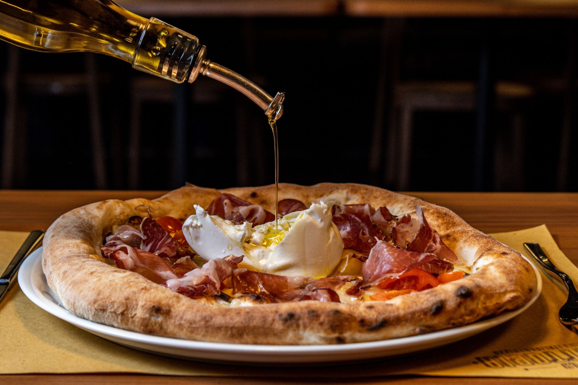 Pizza z serem burrata, szynką parmeńską i oliwą, podana na białym talerzu w restauracji.