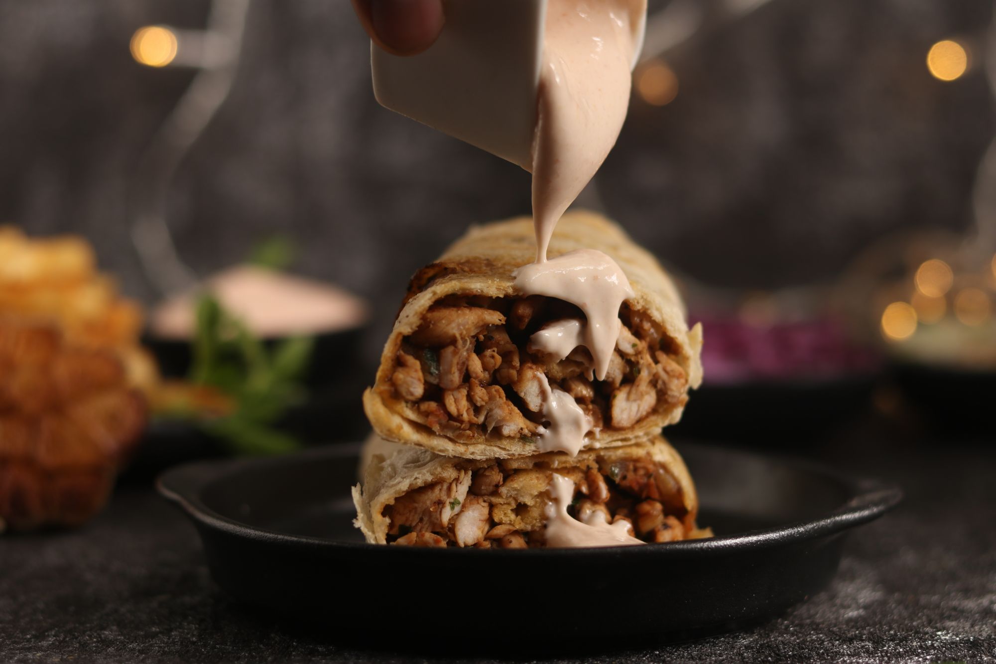 Wyjątkowy kebab w tortilli z mięsem, polany sosem, na czarnym talerzu z bokeh w tle.