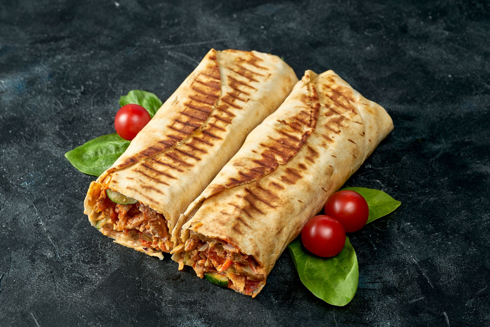Wrap-uri delicioase umplute cu carne și legume, servite cu roșii și frunze de spanac pe o masă întunecată.
