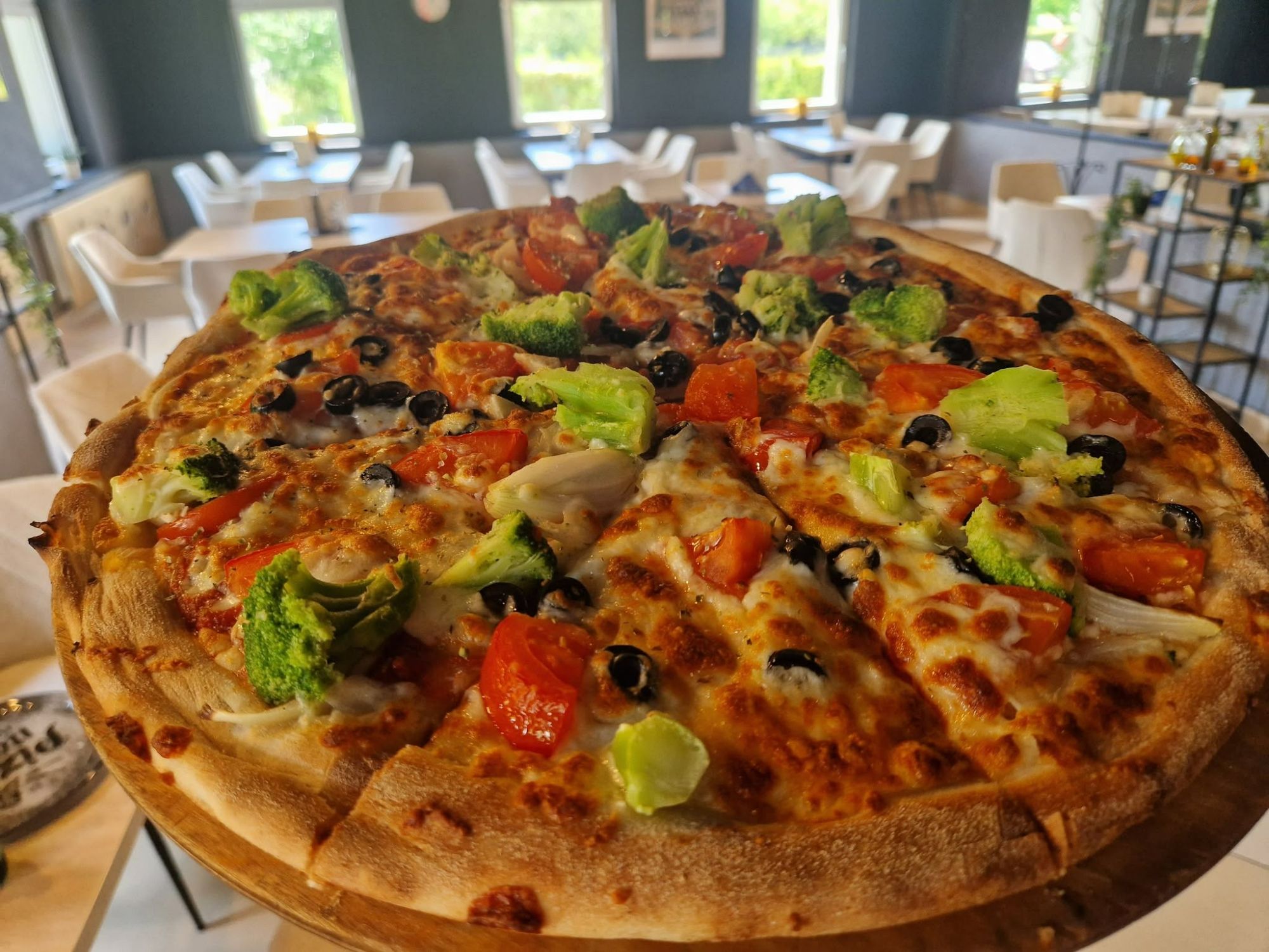 Pyszna pizza z warzywami, serem i oliwkami, na drewnianym talerzu w restauracji z jasnym wnętrzem.