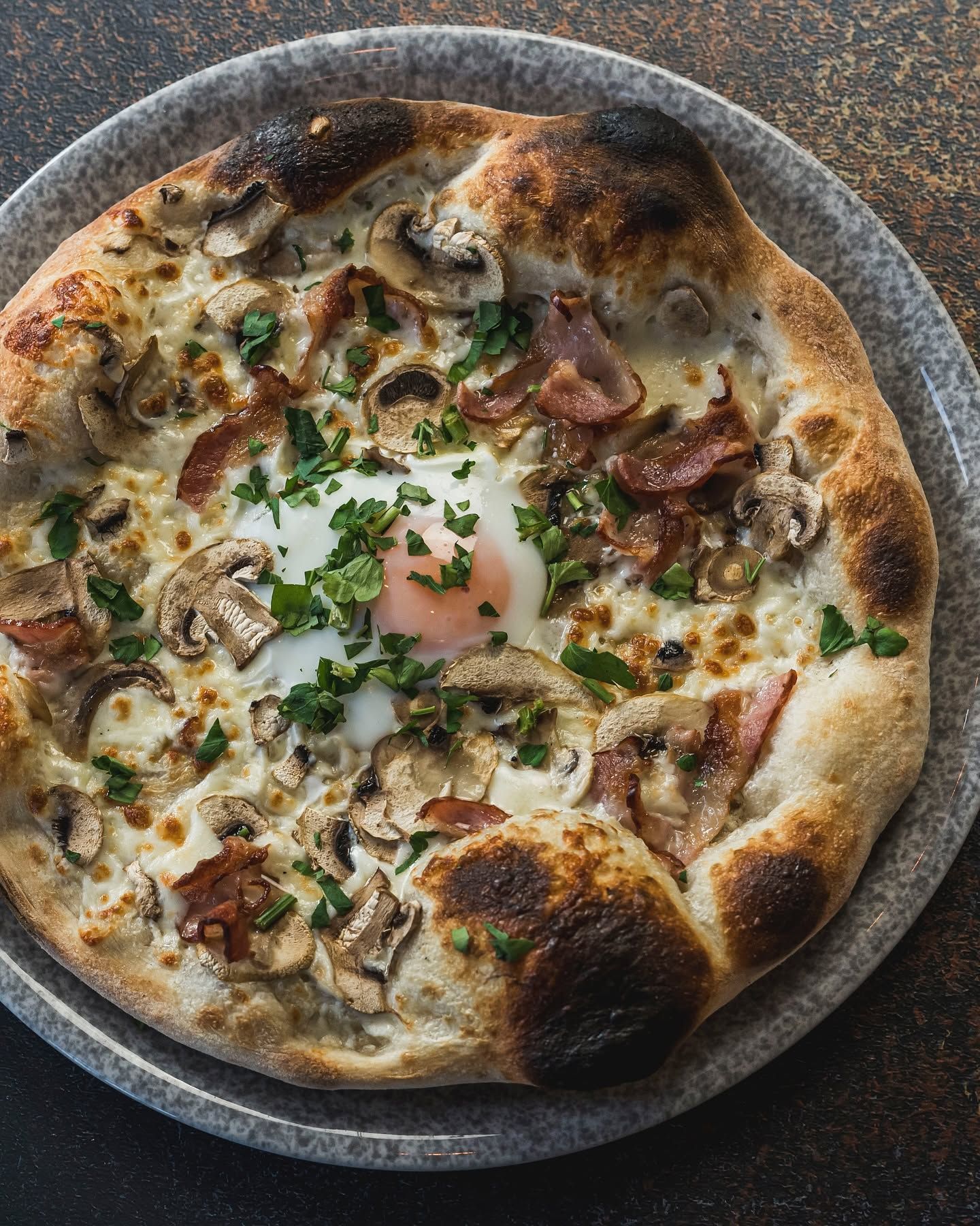 Pizza z jajkiem, szynką, pieczarkami i ziołami na talerzu, z chrupiącym brzegiem.