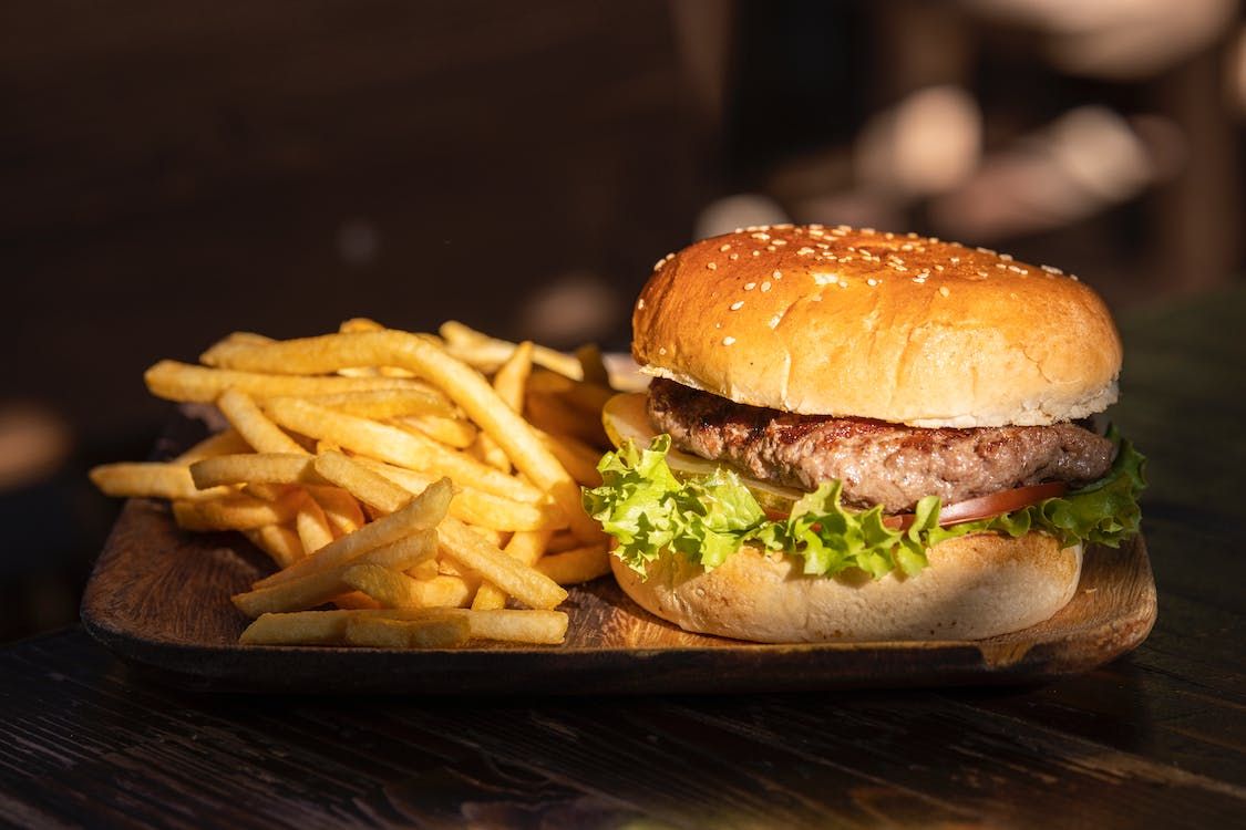 Hamburger z sałatą, pomidorem i cebulą, podany z frytkami na drewnianym talerzu.
