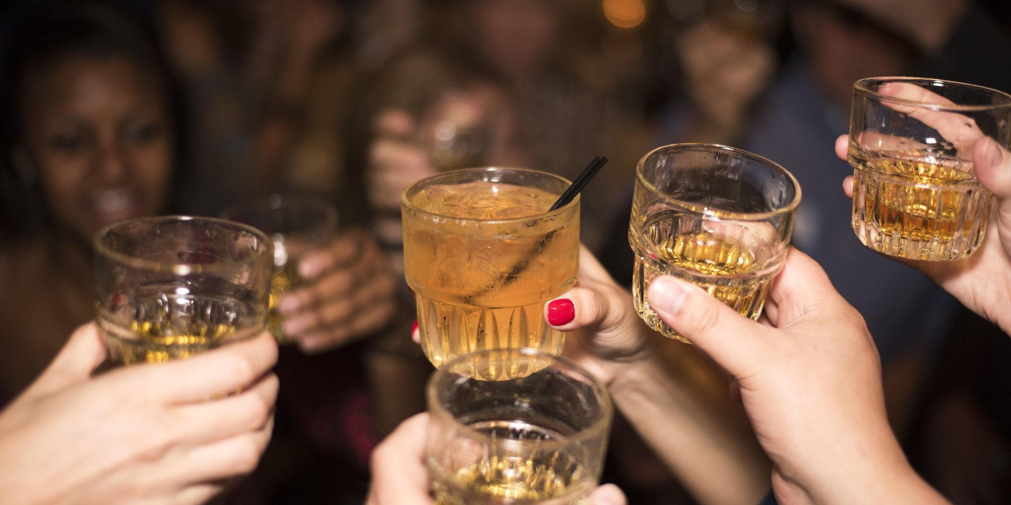 Ręce trzymające szklanki z drinkami, podczas toastu w żywej atmosferze imprezy.