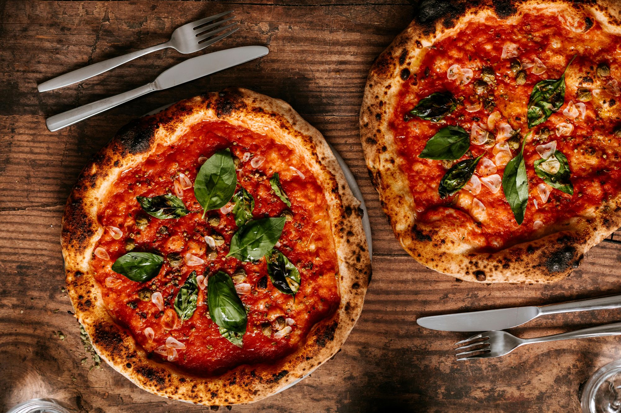 Dwie pizze z sosem pomidorowym, bazylią i przypieczonym brzegiem na drewnianym stole.