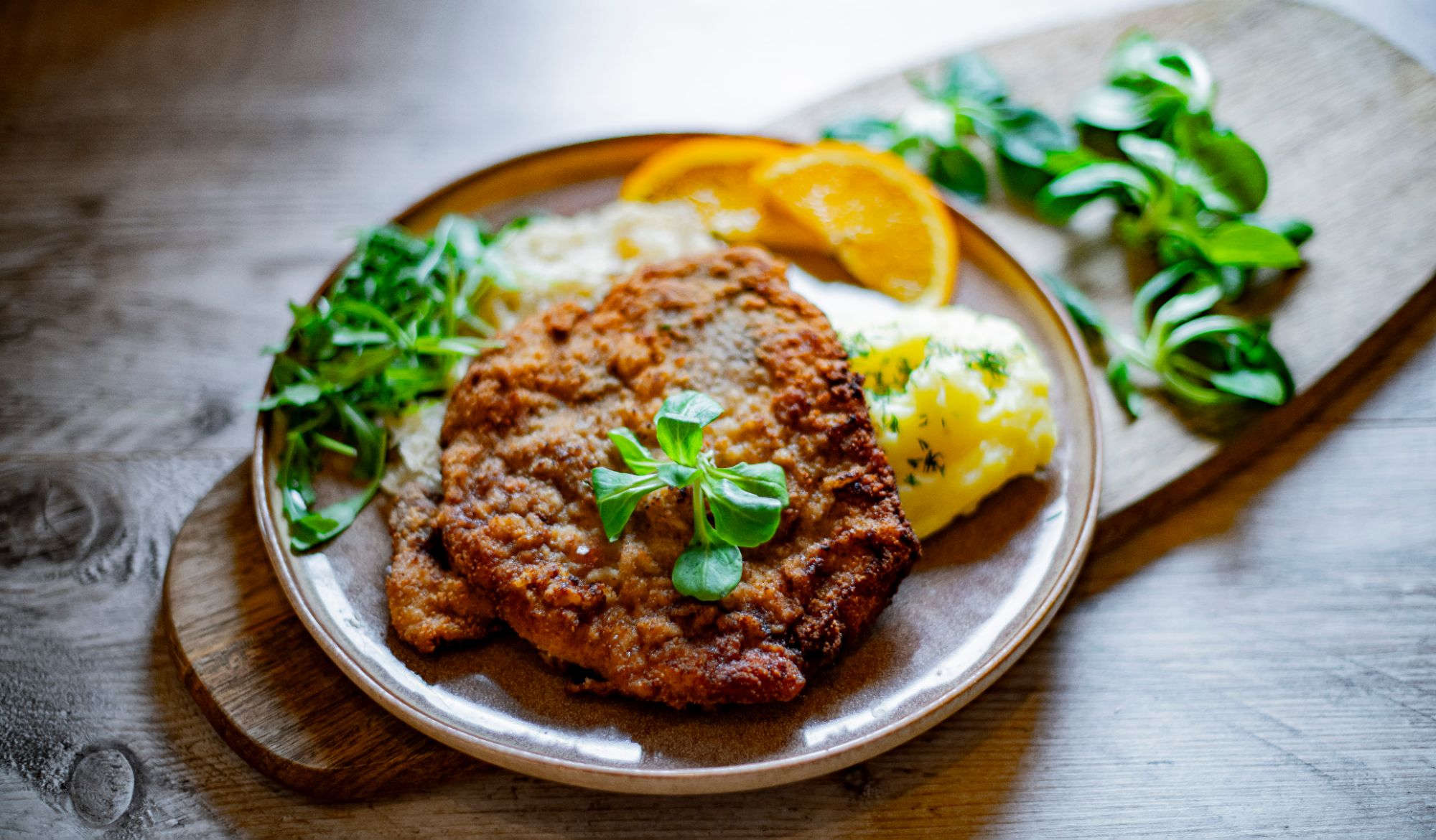 Złoty kotlet schabowy podany z puree ziemniaczanym, kapustą i plasterkami pomarańczy na talerzu.
