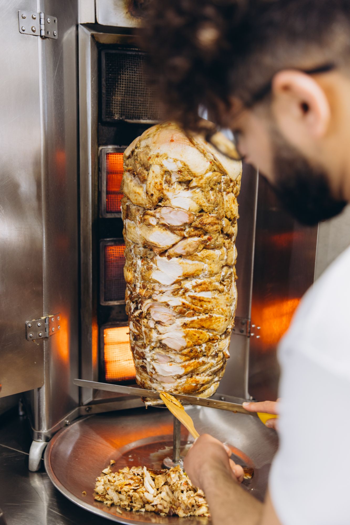 Mężczyzna kroi kebab na rożnie w restauracji, z soczystym mięsem na talerzu.