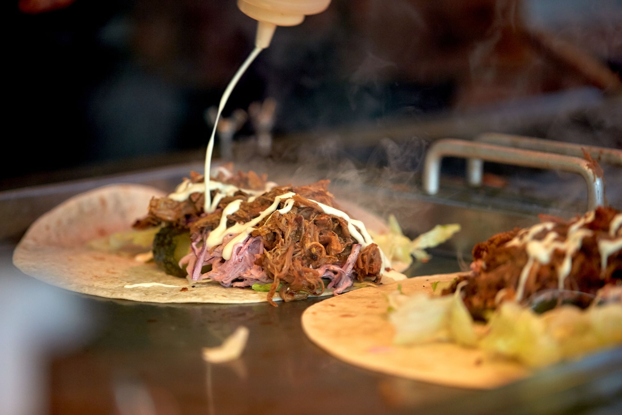 Tortilla z mięsem, sałatą i kapustą, polana sosem, podana na stacji gastronomicznej.