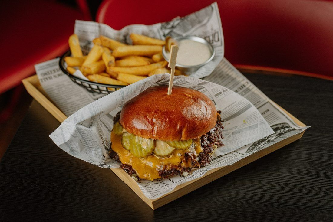 Soczysty burger z serem, piklami i frytkami na talerzu obok, posypany przyprawami.