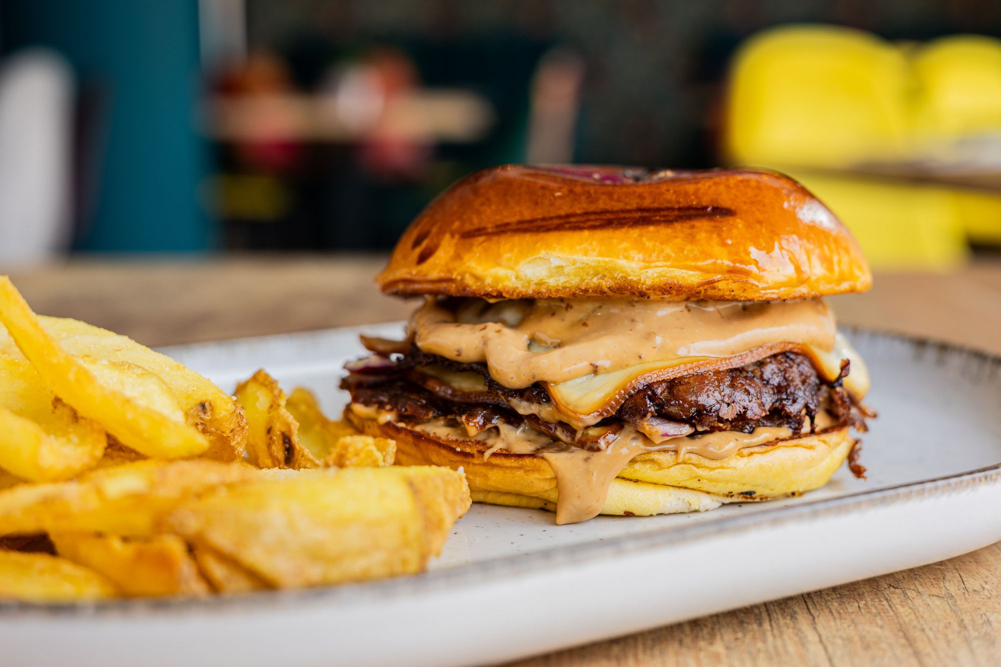 Soczysty burger z wołowiną, serem, sosem na brioche, podany z frytkami na talerzu.