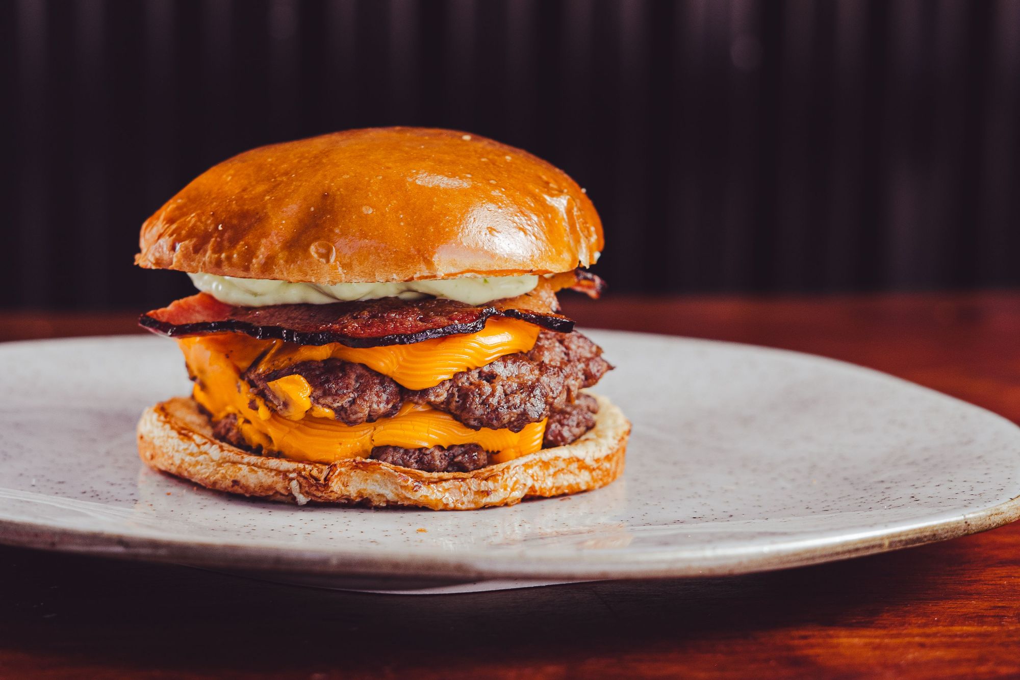 Soczysty burger z serem cheddar, bekonem i majonezem na bułce, podany na talerzu.