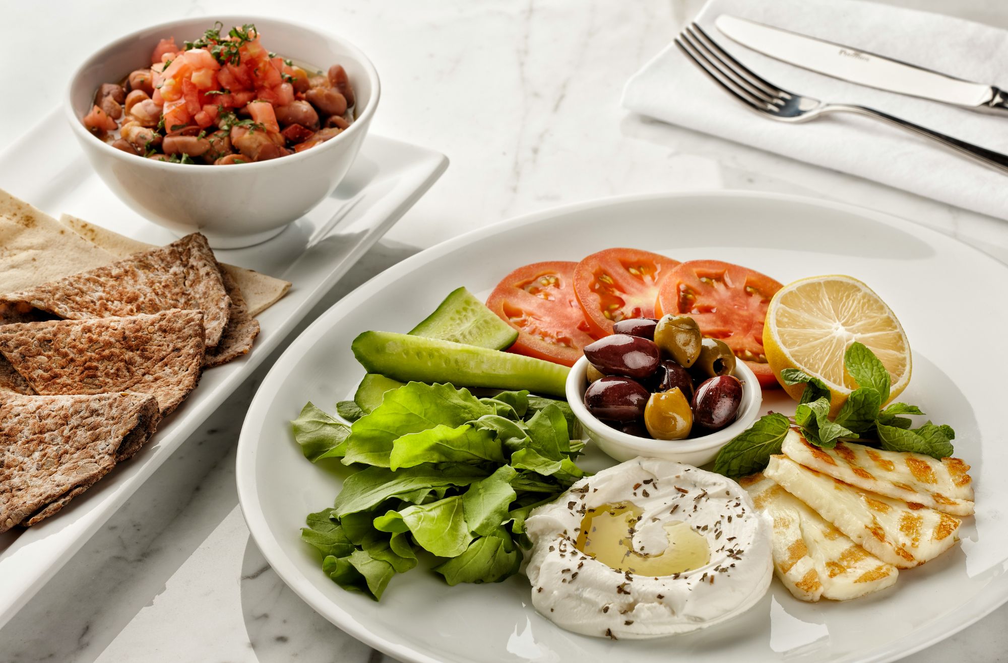 Platou cu salată, roșii, castraveți, măsline, brânză și pâine, alături de salată de fasole și roșii.