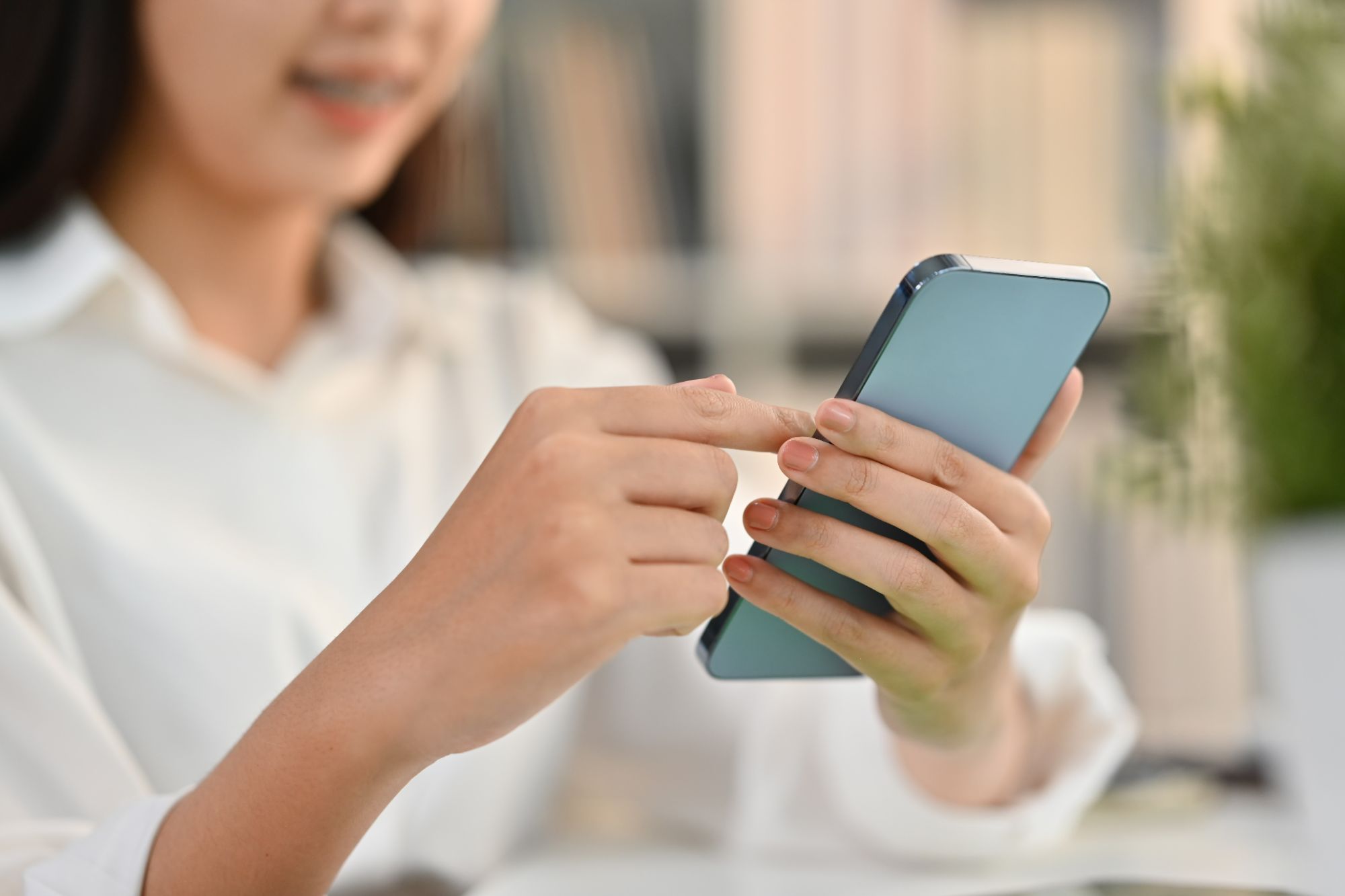 Kobieta trzyma telefon komórkowy i klika na ekranie w biurowym otoczeniu.