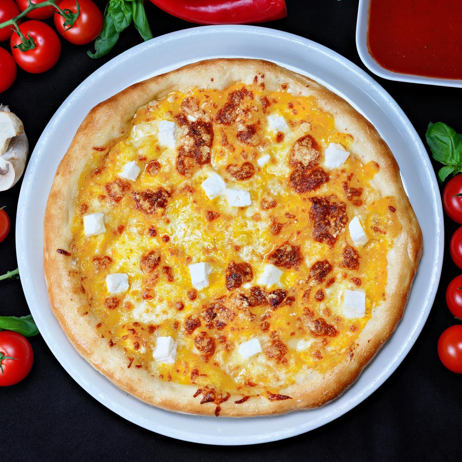 Pizza delicioasă cu brânză, pe o farfurie albă, înconjurată de roșii și ardei.