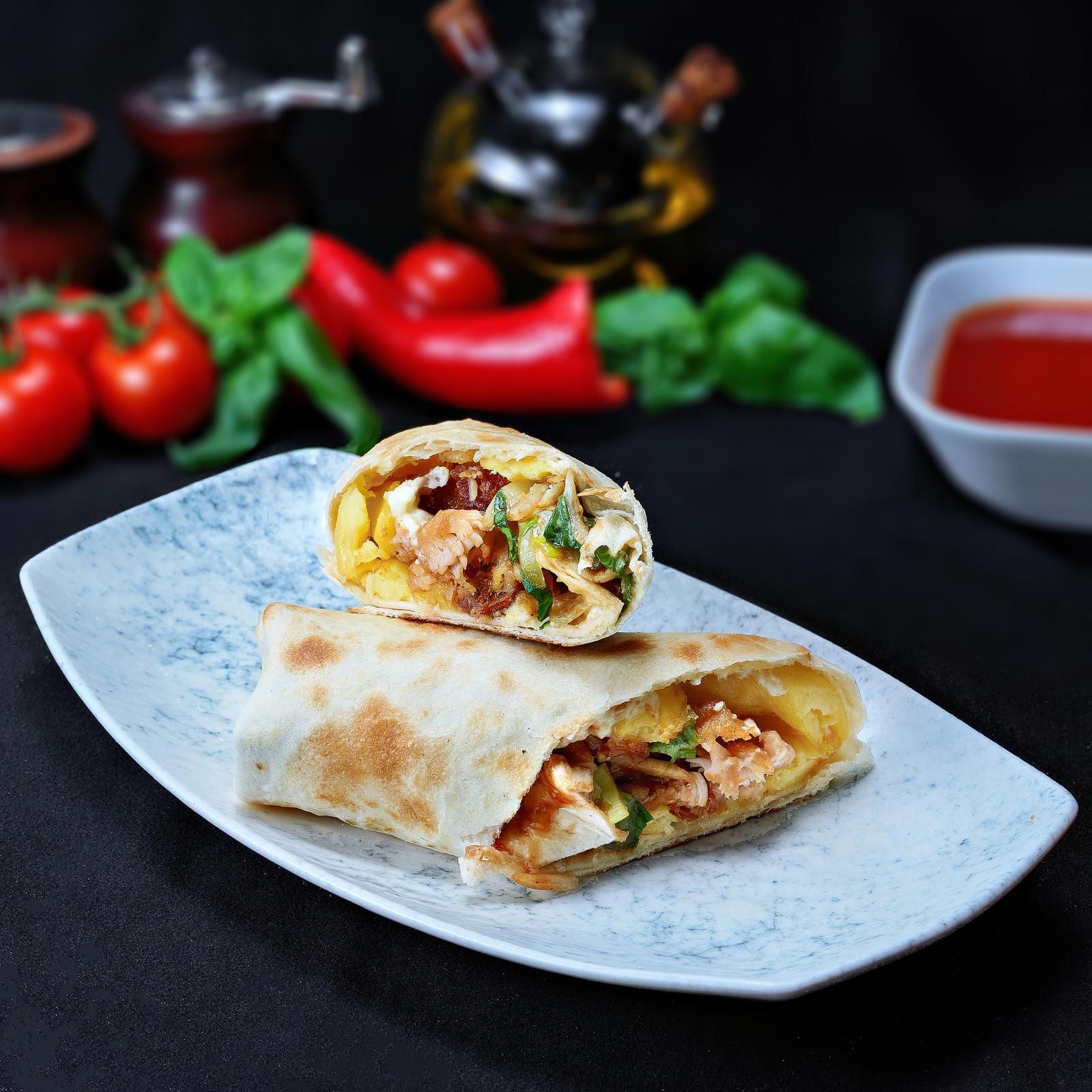 Rulouri delicioase cu carne și legume pe o farfurie, alături de sos și ingrediente proaspete.