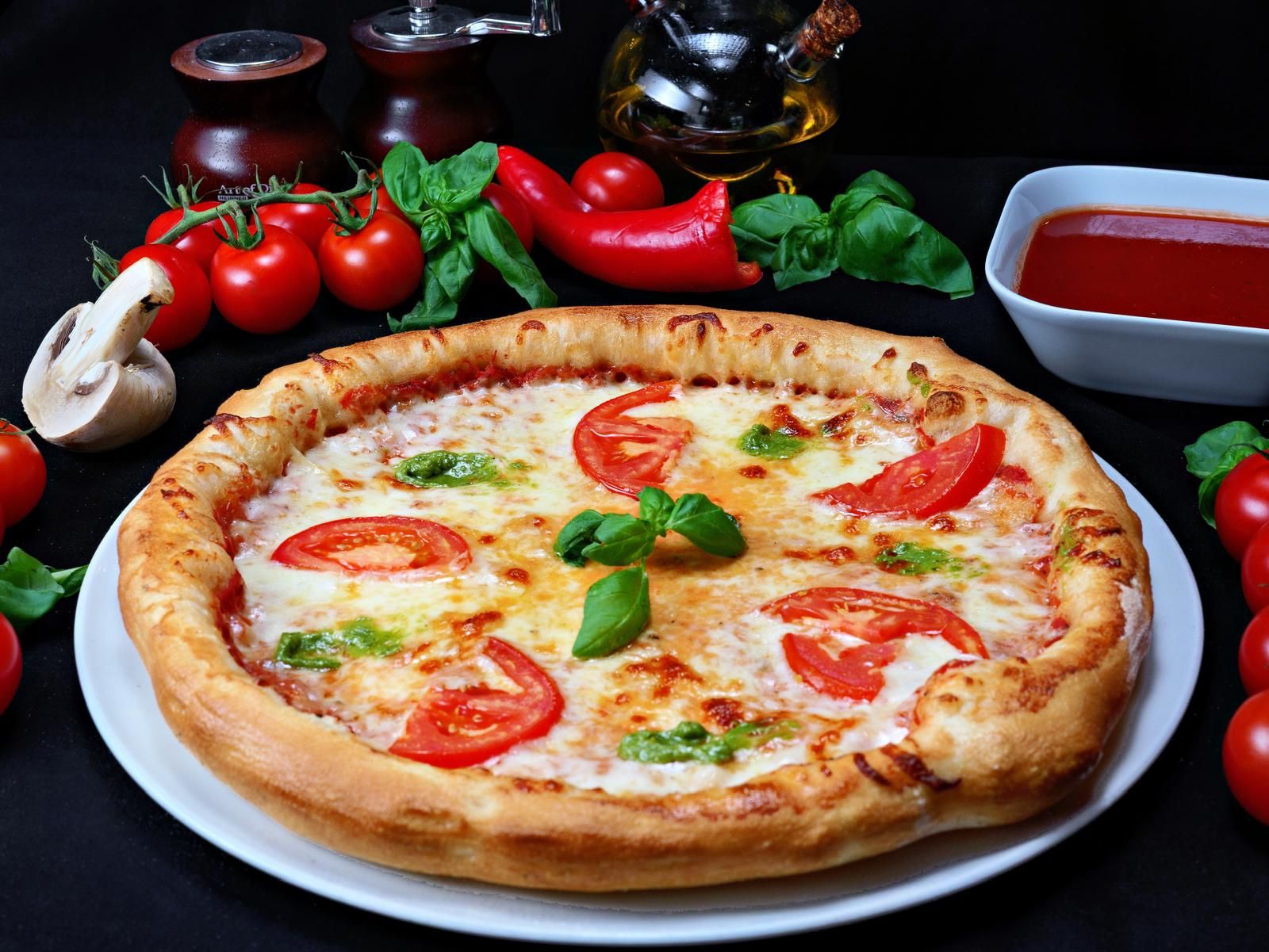 Pizza Margherita cu roșii, mozzarella și busuioc, înconjurată de ingrediente proaspete.