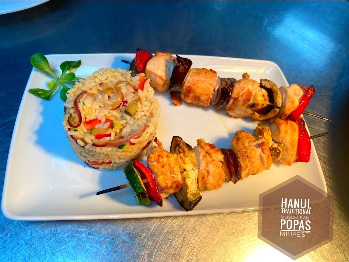 Souvlaki cu pui, legume și orez cu legume, servit pe o farfurie albă.