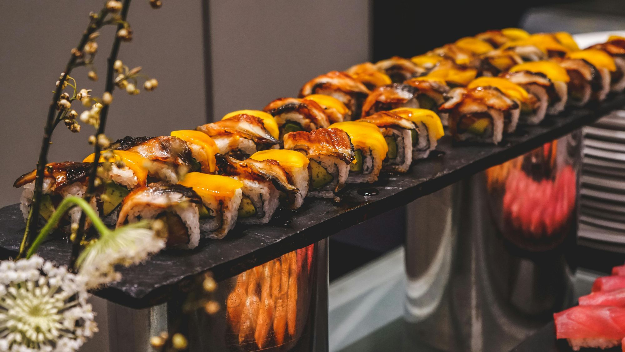 Estetyczna deska sushi z różnymi rolkami, dekorowana kwiatami i soczystym owocem.