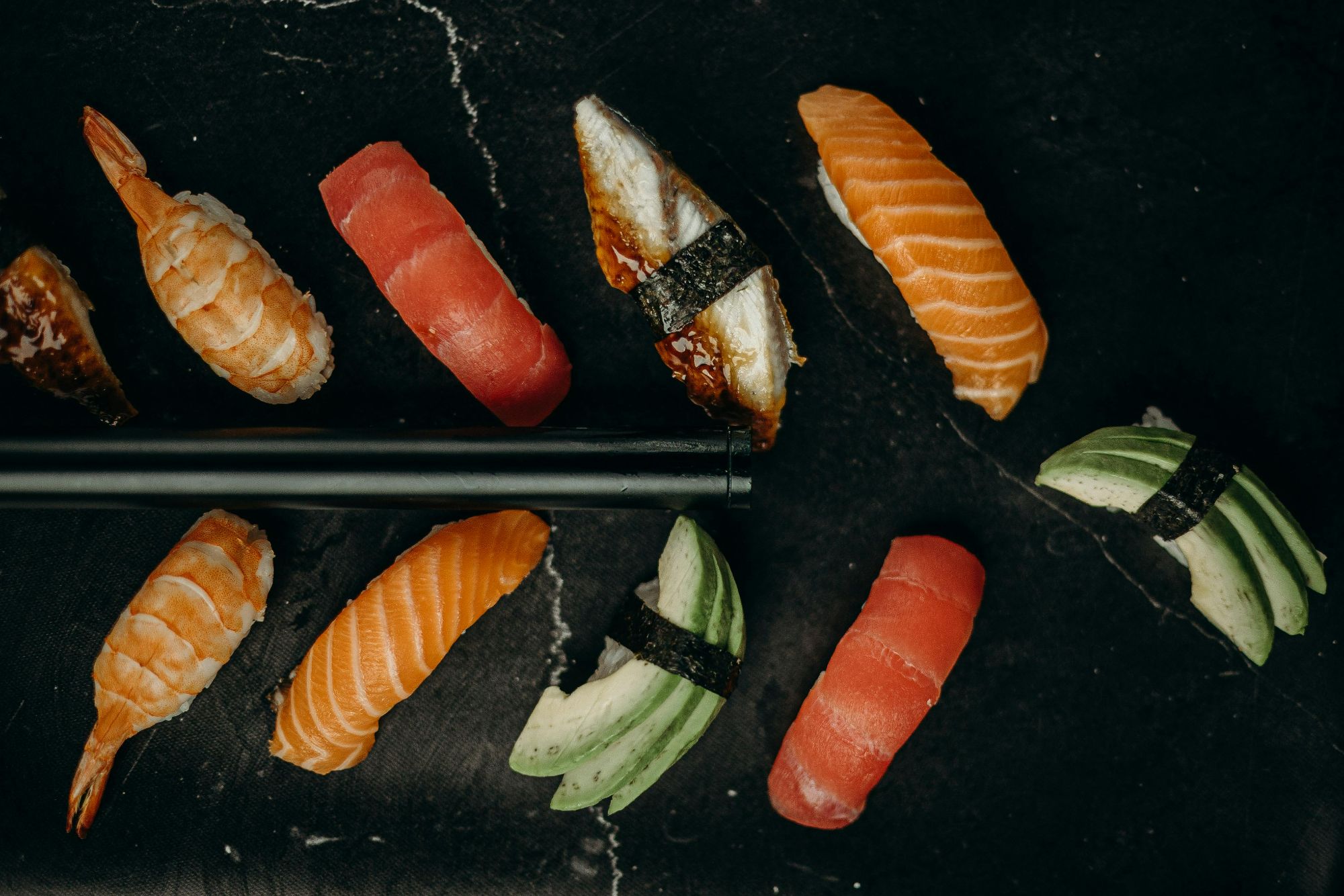 Różnorodne sushi na czarnym tle z pałeczkami, w tym łosoś, tuńczyk i krewetki.